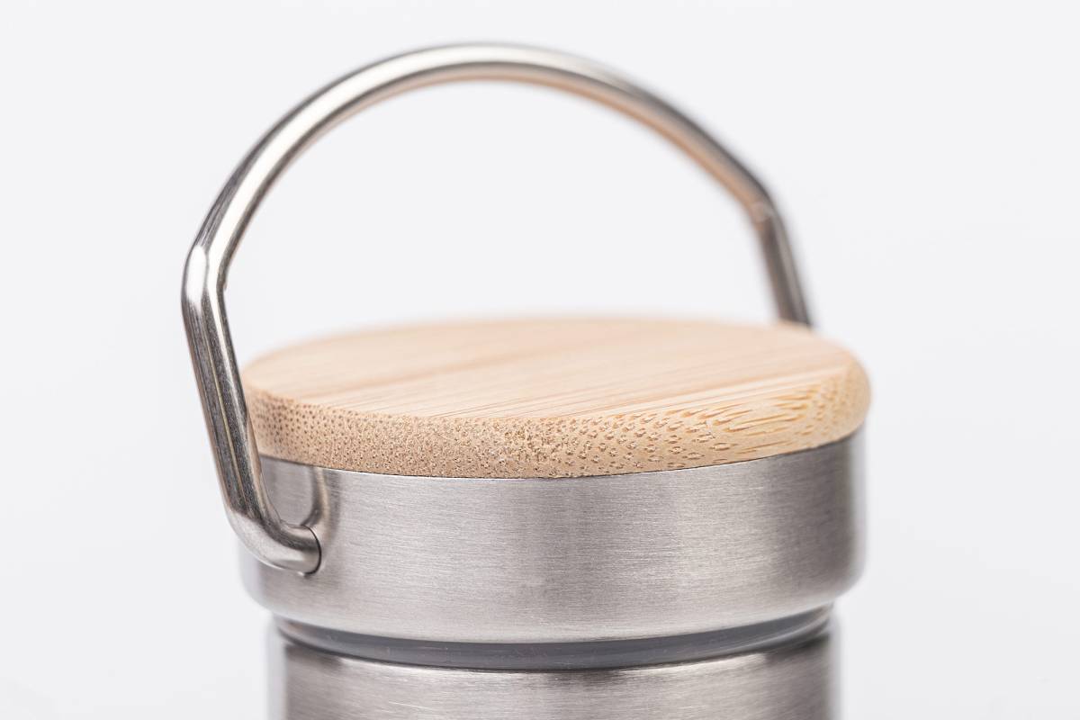 Detailaufnahme des Schraubdeckels einer Edelstahl-Trinkflasche mit flacher Bambusoberfläche und stabilem Metallbügelgriff, auf neutralem Hintergrund.