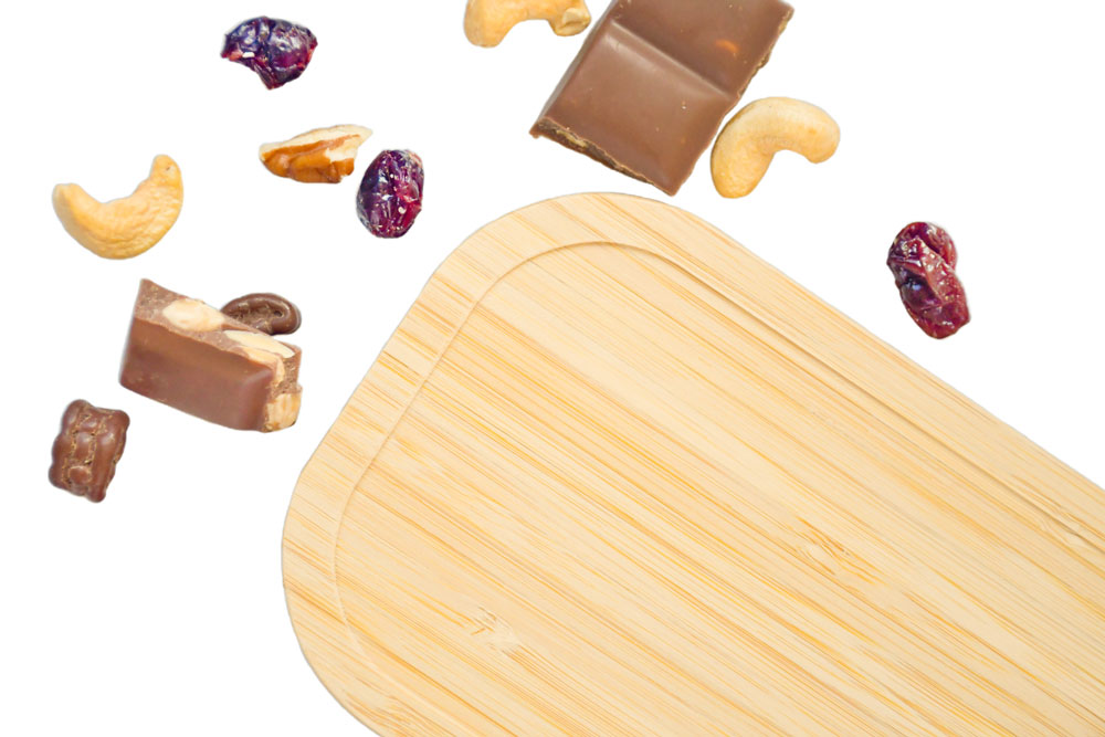 Sustainable bamboo lid as a replacement part for tinplate lunchbox, surrounded by trail mix and chocolate