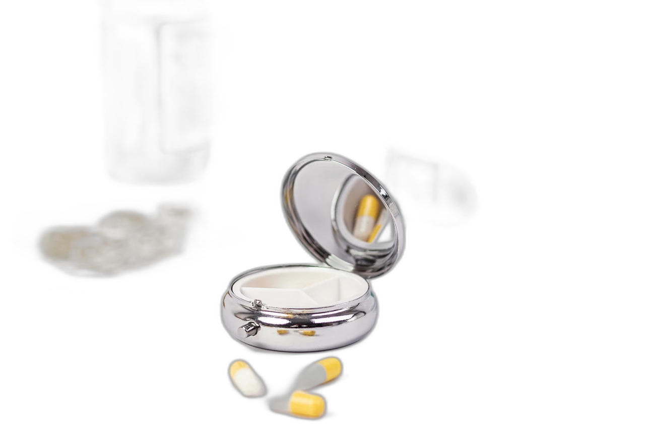 Geöffnete runde Pillendose aus silberfarbenem Metall mit drei Innenfächern und integriertem Spiegel, fotografiert mit Tabletten und Medizin im Hintergrund.