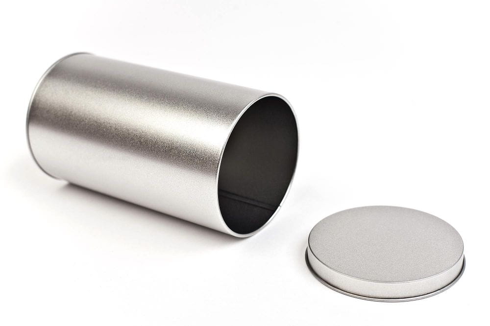 Geöffnete runde Blechdose aus silberfarbenem Metall mit abgenommenem Stülpdeckel, auf weißem Hintergrund fotografiert.