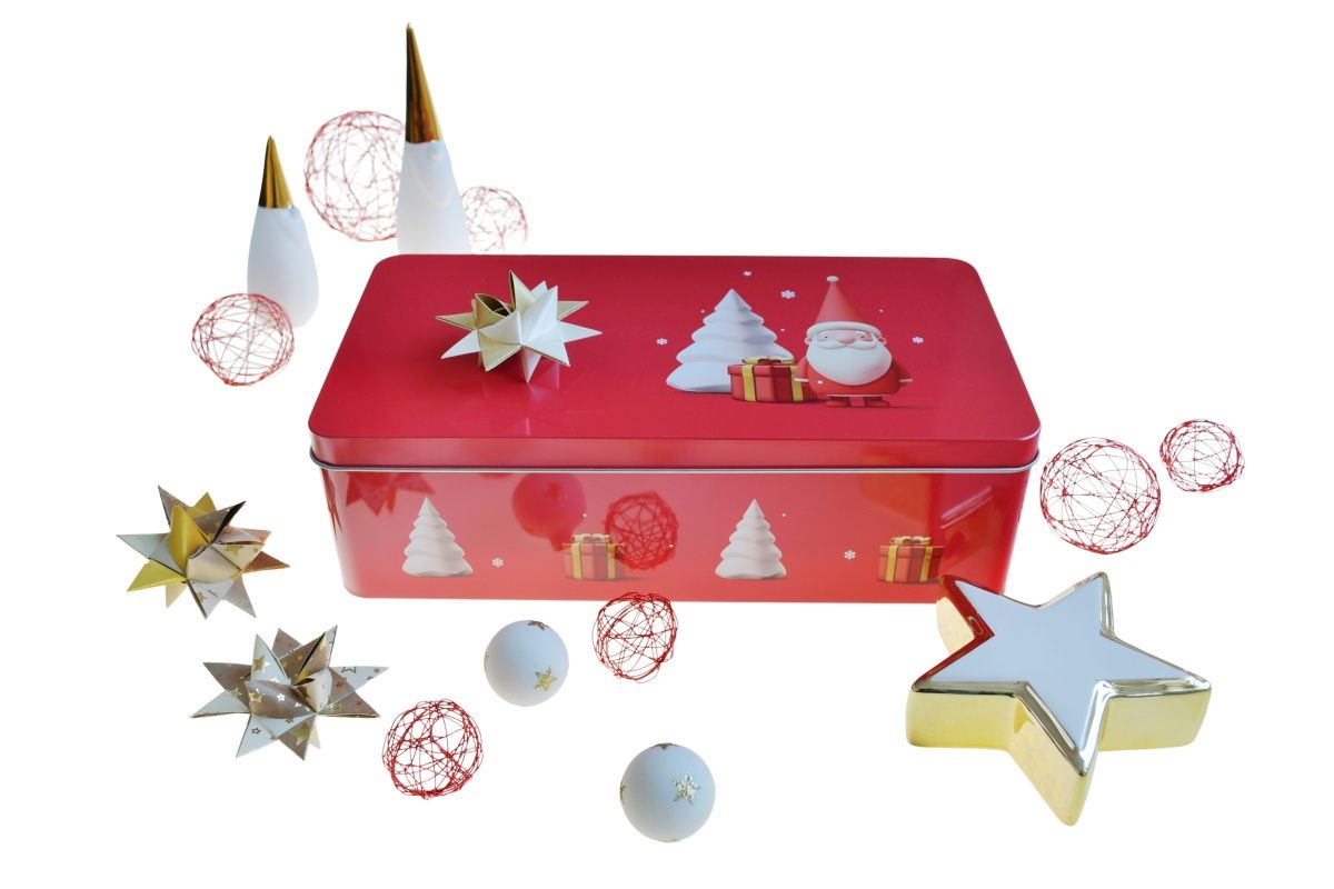 Rote Weihnachtsdose aus Metall mit Weihnachtsmotiven (Santa und Tannenbäume) auf dem Deckel, umgeben von Weihnachtsdekor wie goldenen und weißen Sternen, roten Drahtbällen und Kugeln, neutraler Hintergrund.