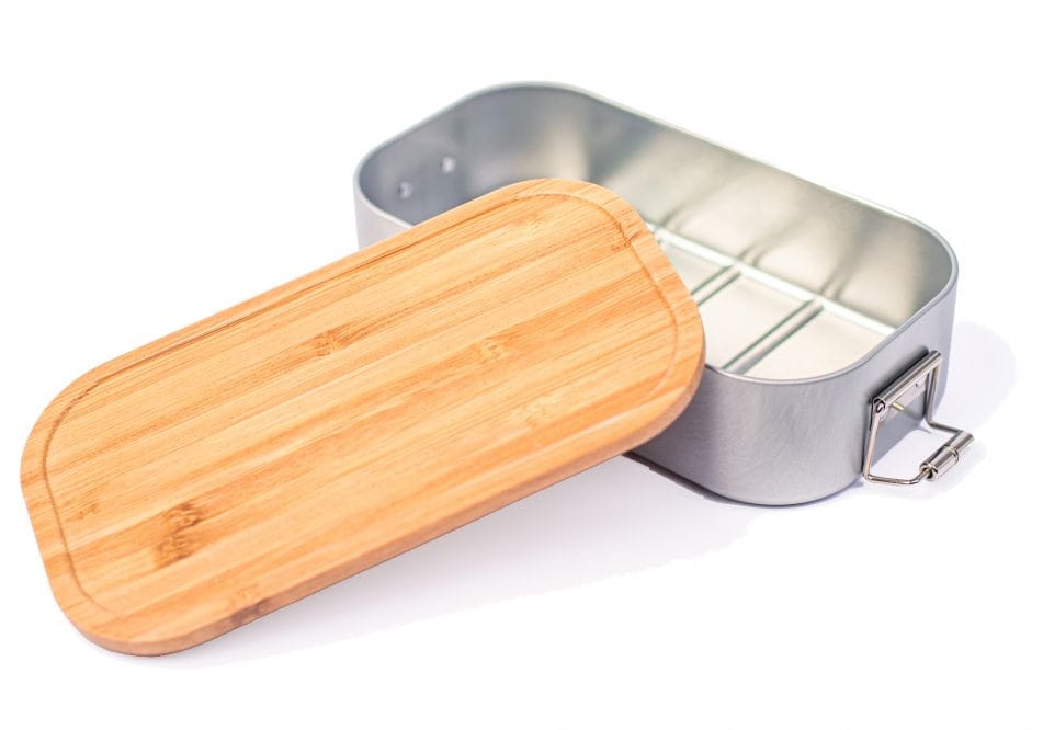 Geöffnete rechteckige Lunchbox aus silberfarbenem Metall mit seitlichen Clips und aufgelegtem Bambusdeckel, auf weißem Hintergrund fotografiert.